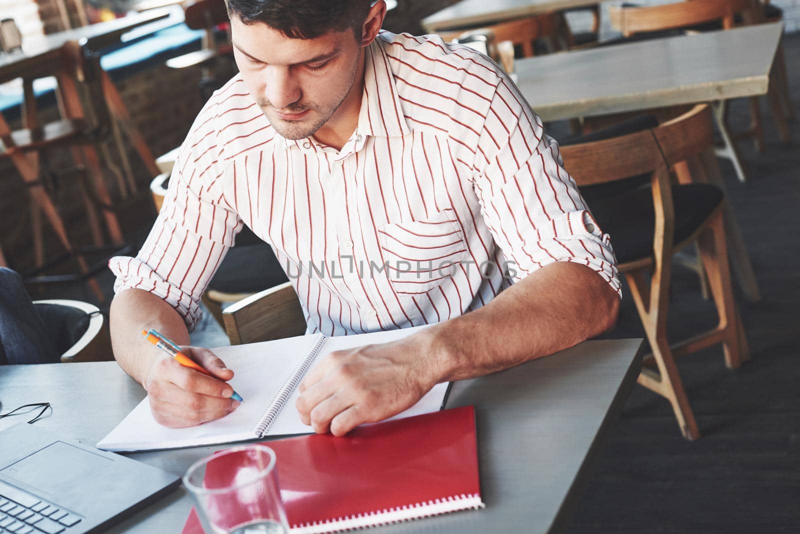 Making some corrections. Adult man sits in cafe at daytime and making reports in notepad with laptop on the table.
