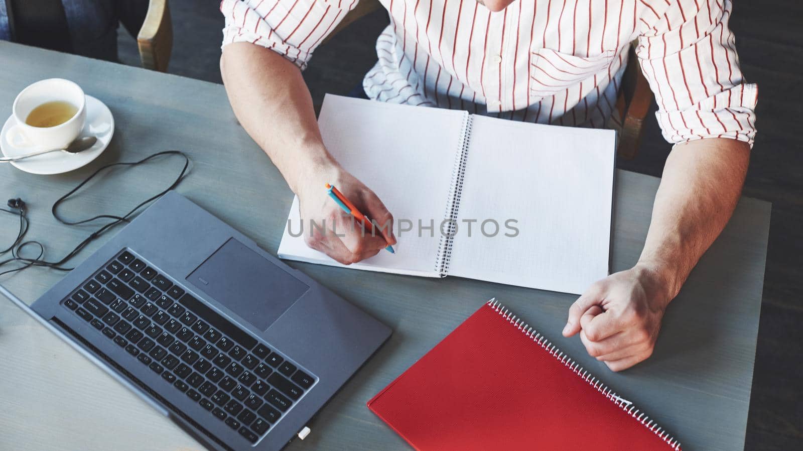 Job is going on. Particle view of freelance man working on the project with laptop and notepads on table.