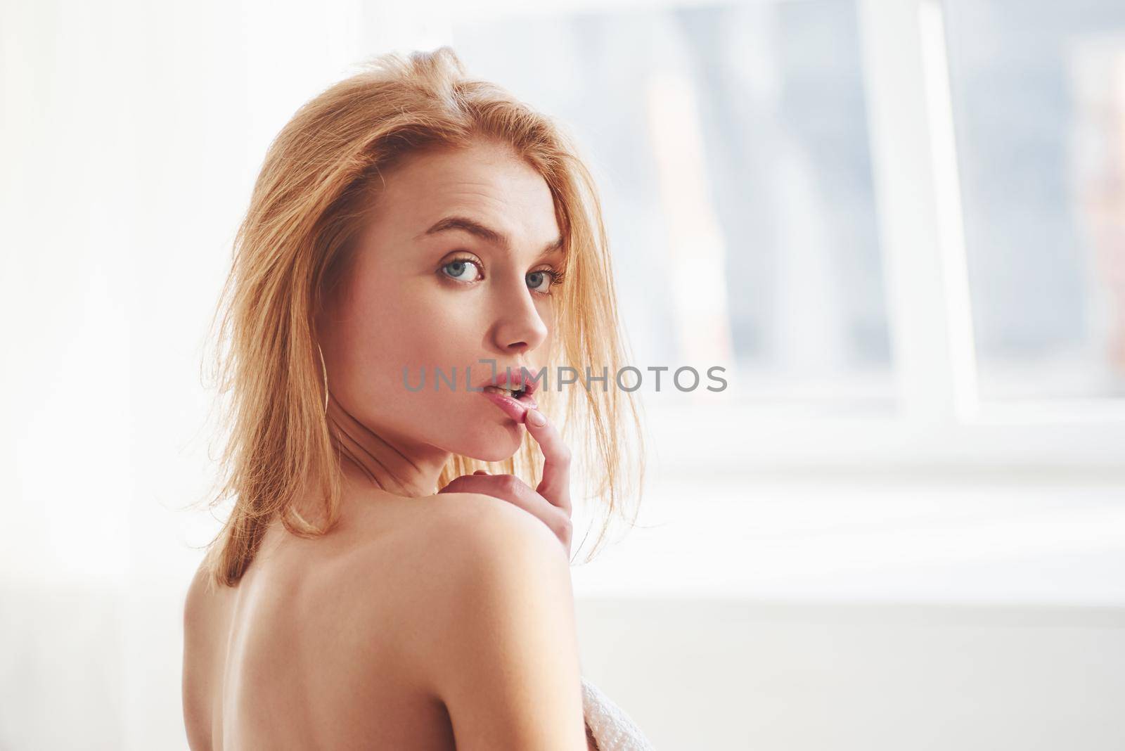 Touching lips with finger and looks away. Portrait of sexy redhead girl stands indoors and looking into the camera.