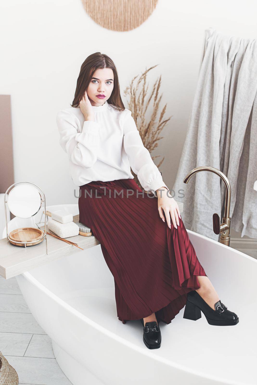 Portrait of fashionable women in red skirt, white blouse and stylish black high-heeled shoes with a buckle posing in a bath. Girl with a big red lips