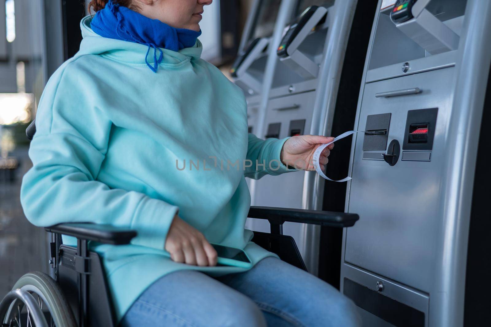 Caucasian woman in a wheelchair buys a ticket at a self-service ticket office. by mrwed54