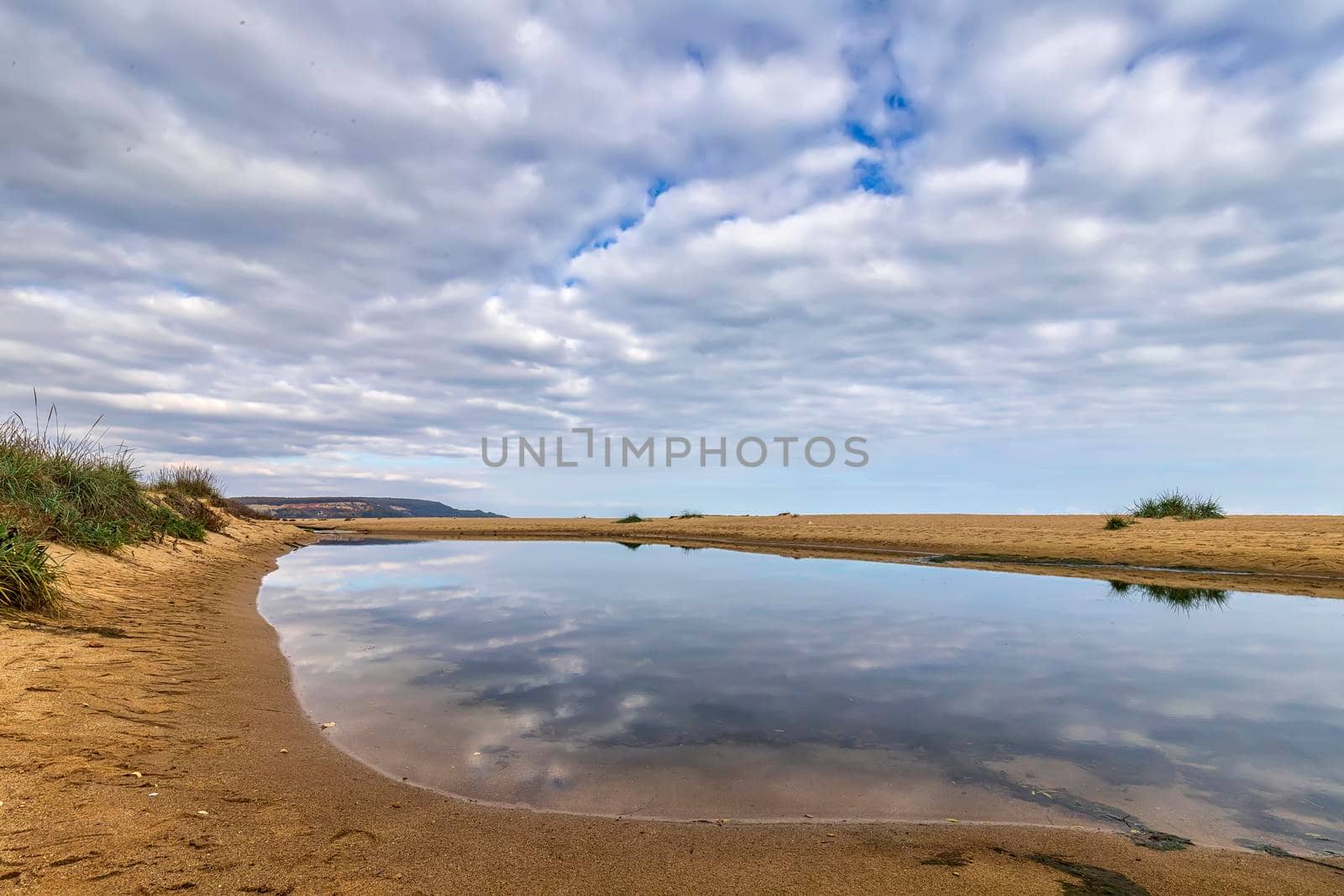 Small lake near sea sand with sky reflection