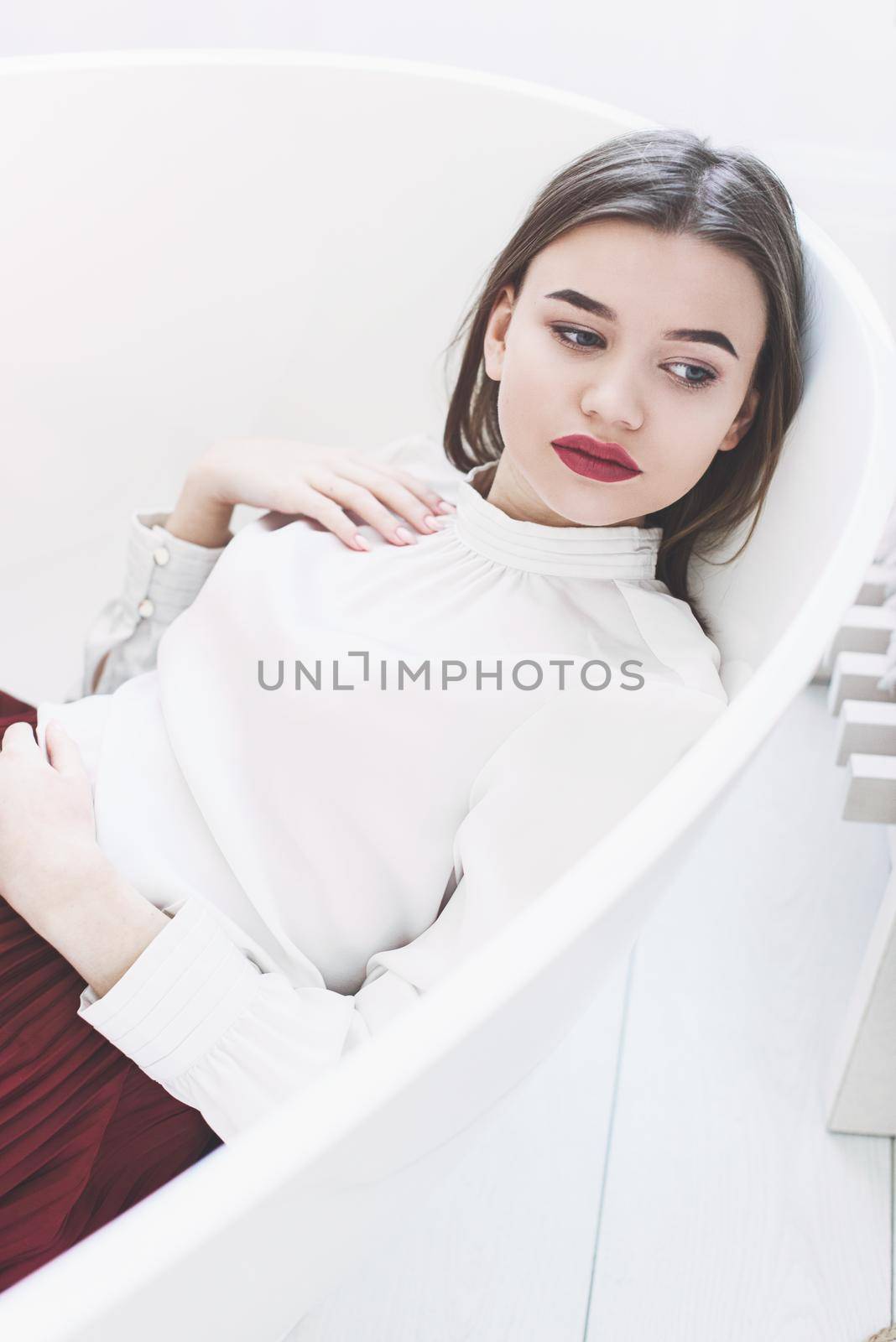 Portrait of fashionable women in red skirt and white blouse posing in a bath. Girl with a big red lips