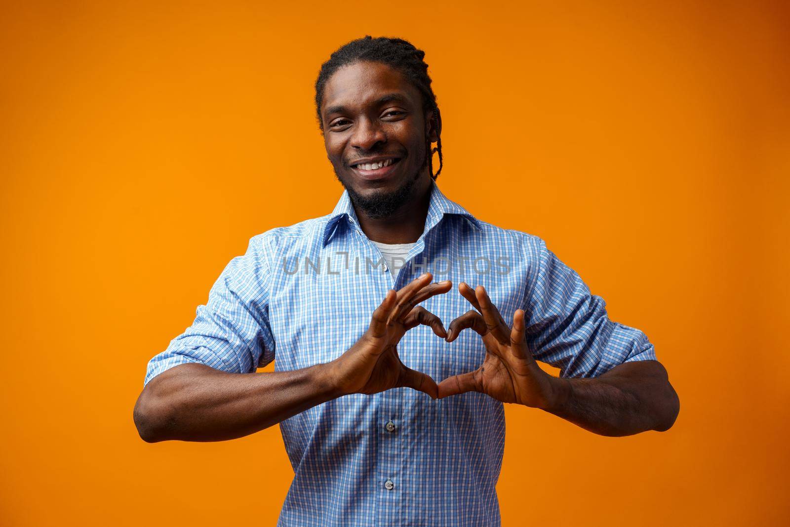 Young black man doing a heart sign over yellow background, close up