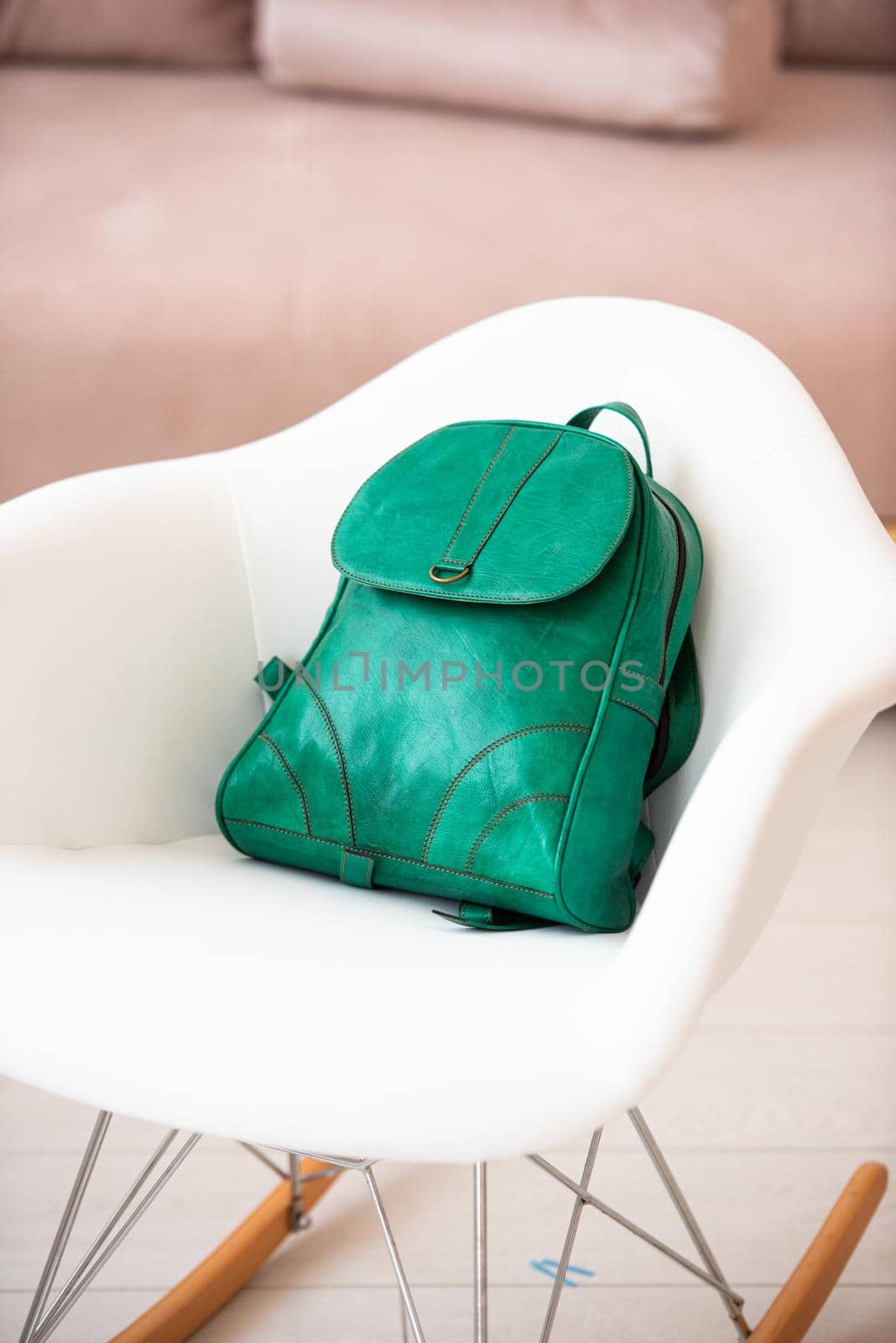 A green leather modern backpack on a white chair. Indoors