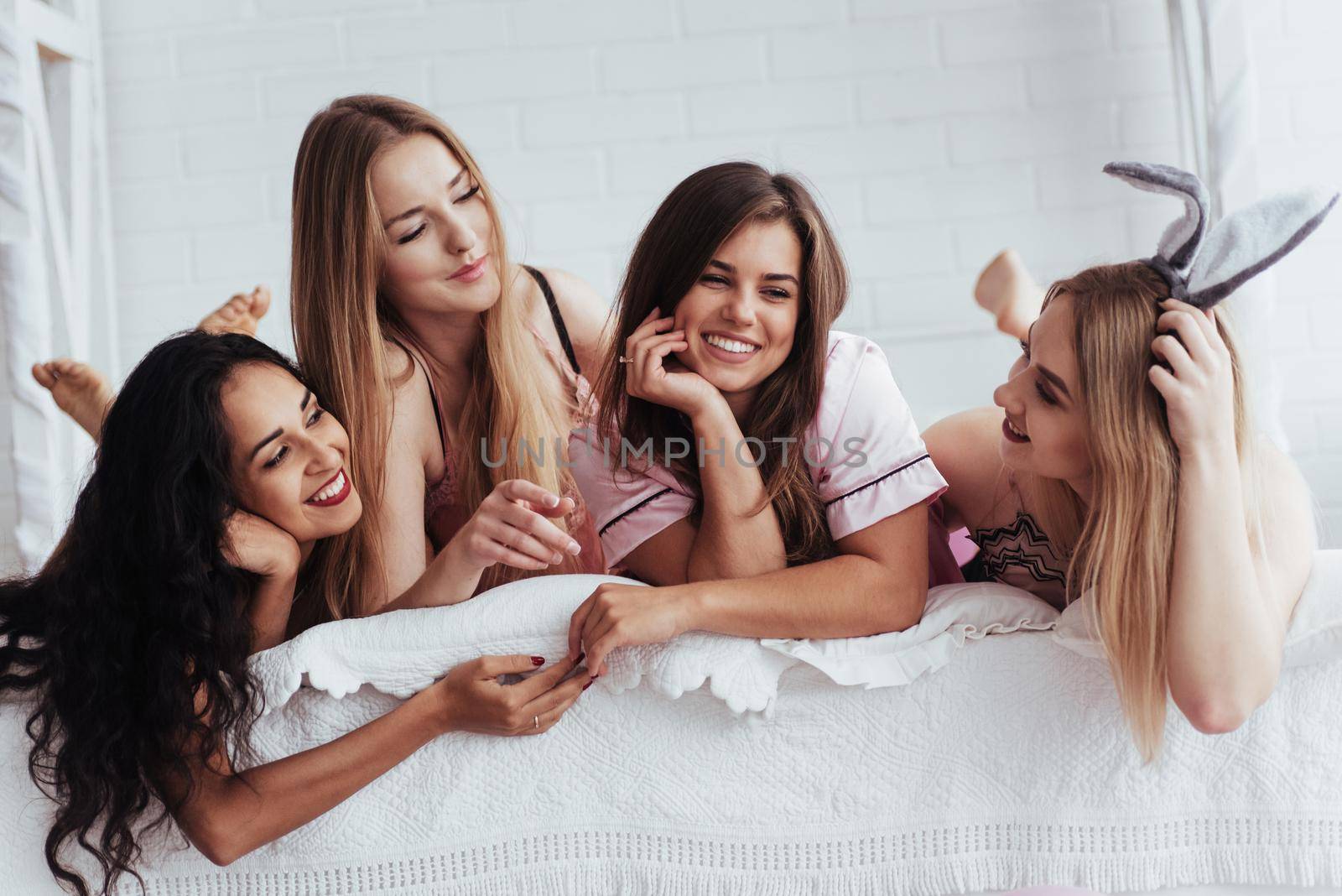 Having friendly conversation. Joyful girls in the nightwear lying on the bed in white room and have celebration.