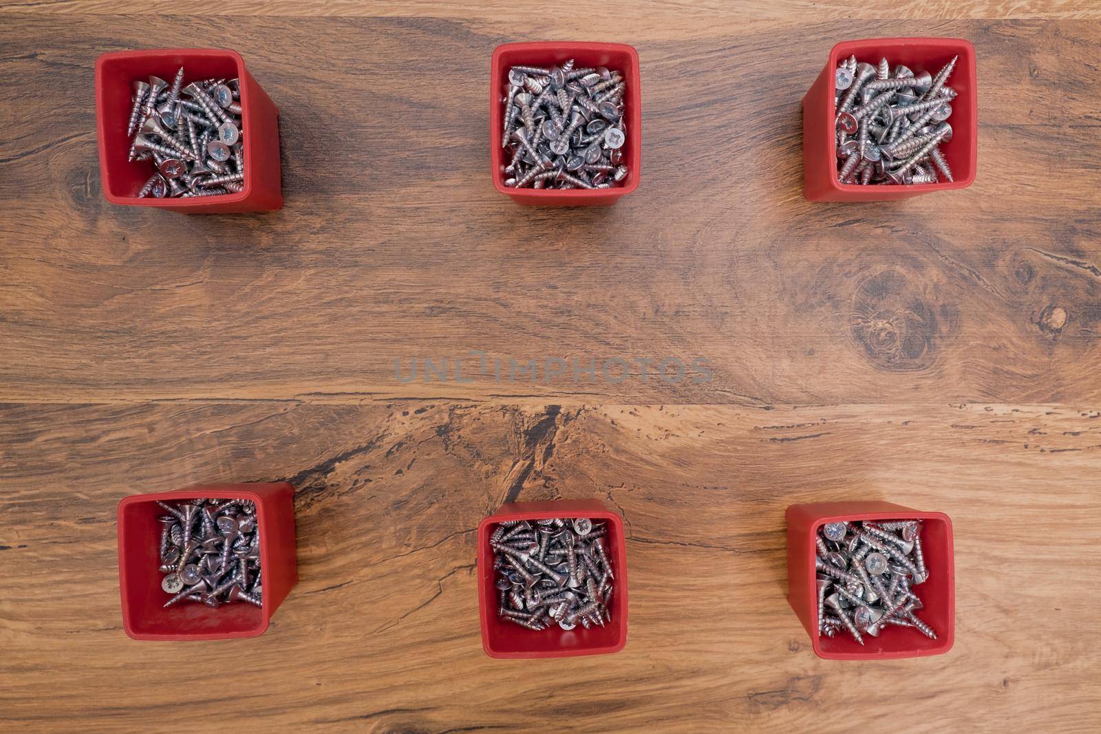 Various size and shape of screws selection in red plastic tray box with cope space on a wooden background.