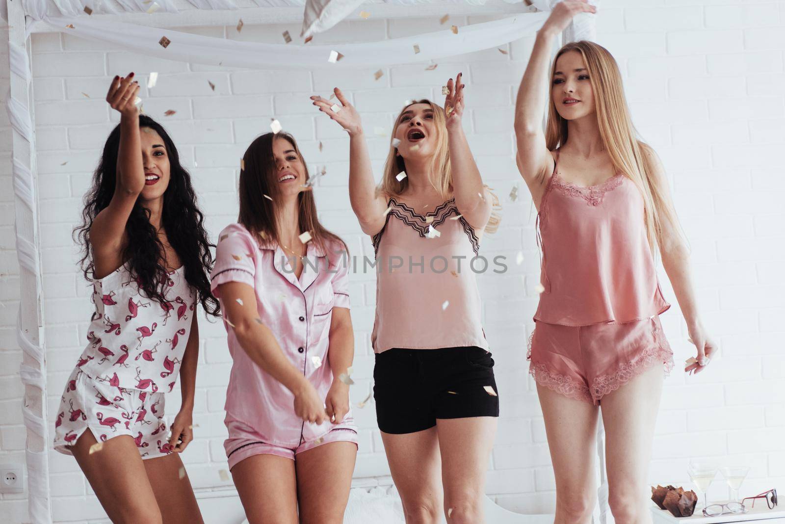 Look at these flying things. Confetti in the air. Young girls have fun on the white bed in nice room by Standret