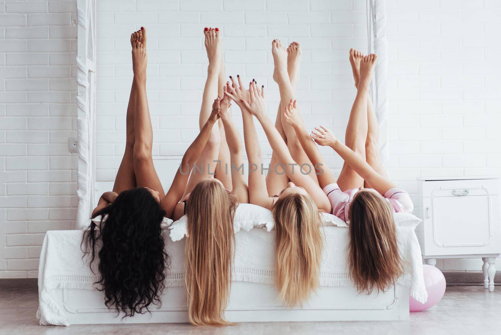 Touching with hands. Four young women with good body shape lying on the bed with their legs up by Standret