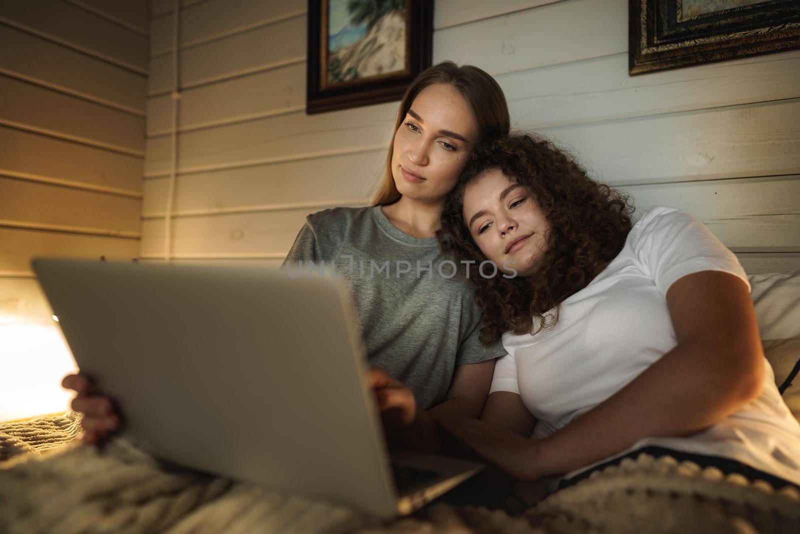 Two beautiful women lying in bed and watching movies on laptop at home