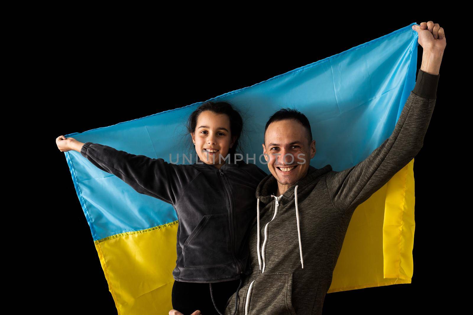 Little girl holding Ukrainian flag hugging her dad on the dark background. Stand with Ukraine. by Andelov13