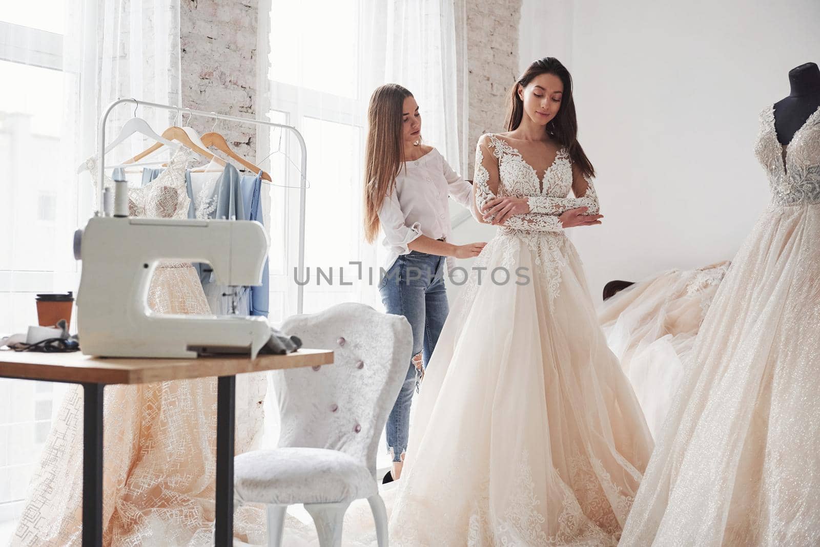 Girl is helping bride. The process of fitting the dress in the studio of hand crafted clothes.