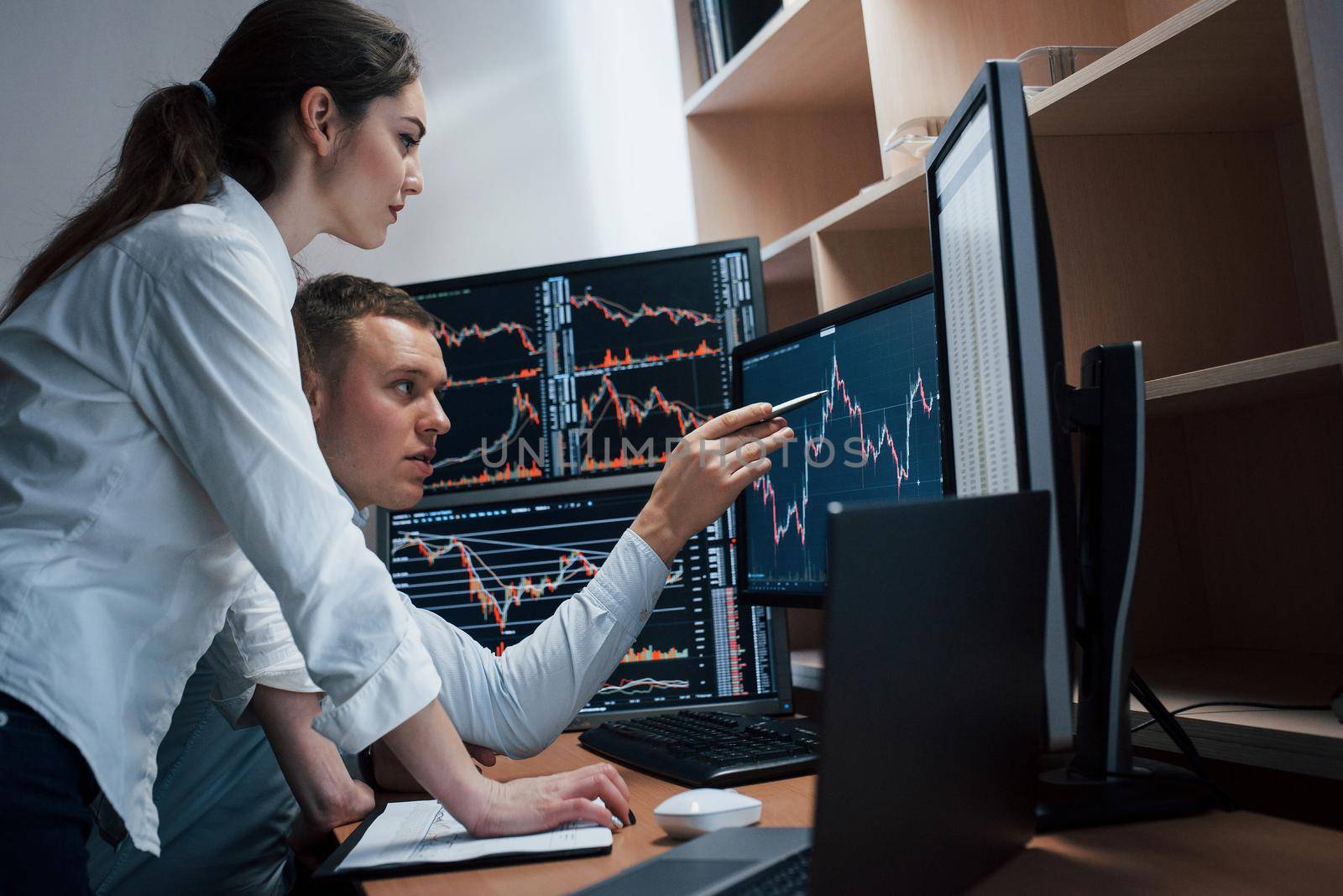 Team of stockbrokers are having a conversation in a office with multiple display screens.