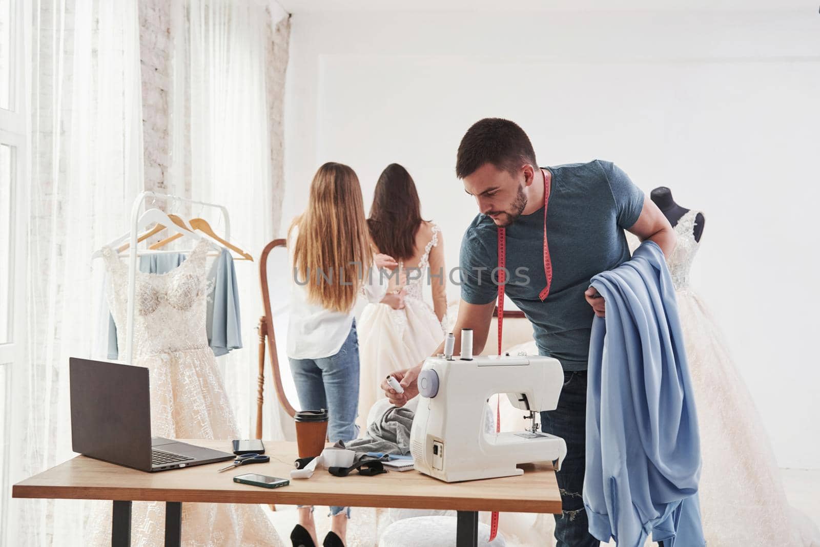 Guy holds cloth and takes some instruments for work. The process of fitting the dress in the studio of hand crafted clothes.