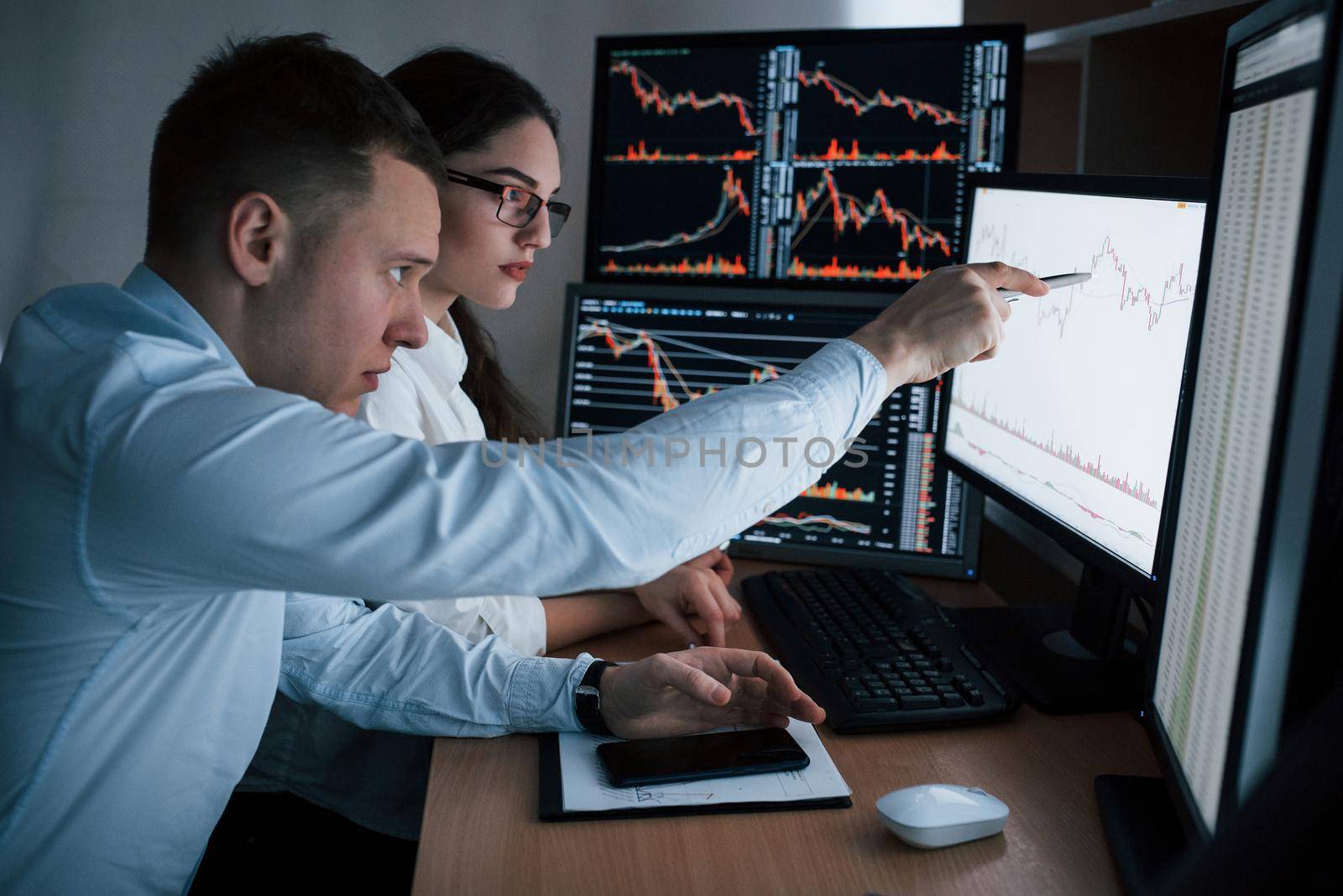 Planning the business project. Team of stockbrokers are having a conversation in a office with multiple display screens.