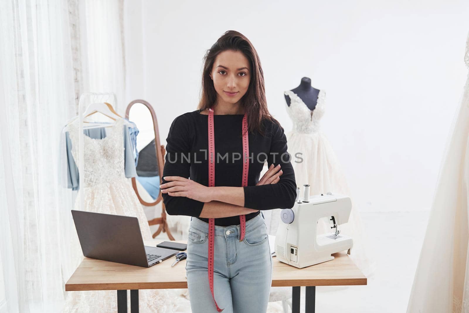 Conception of the wedding clothes. Portrait of female fashion designer standing in the workshop and table with instruments behind.
