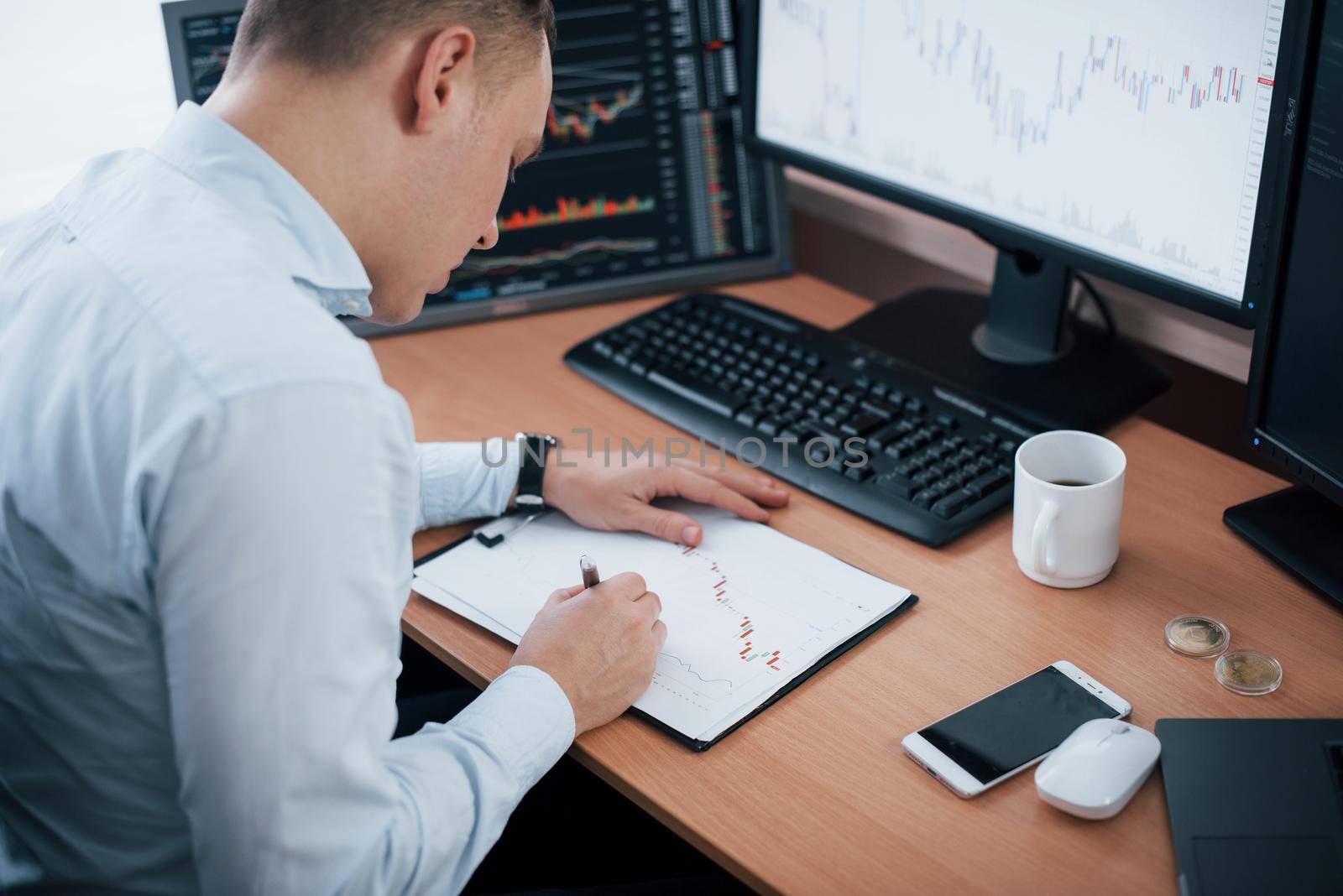 Corrections on the graphs on paper. Man working online in the office with multiple computer screens in index charts.