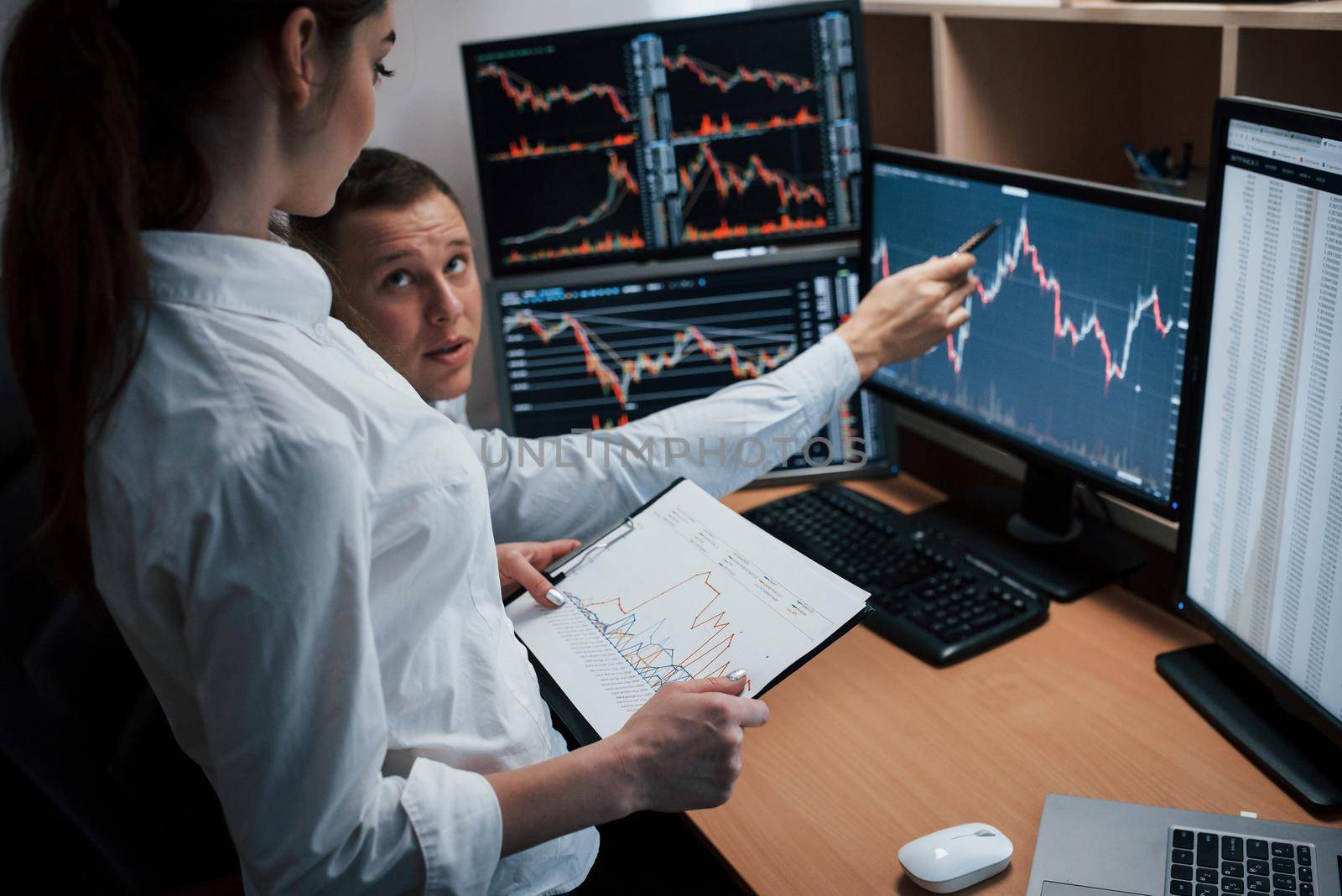 Reaching point of these two employees. Team of stockbrokers are having a conversation in a office with multiple display screens.