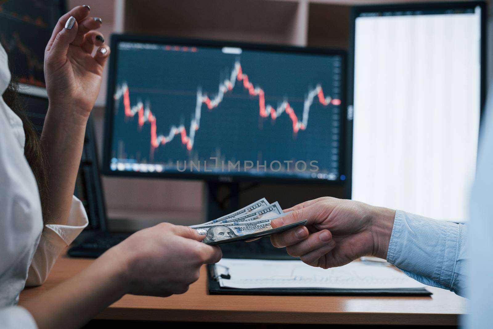 Man gives money to a woman. Day of salary in the modern office with screens with graphs on them.