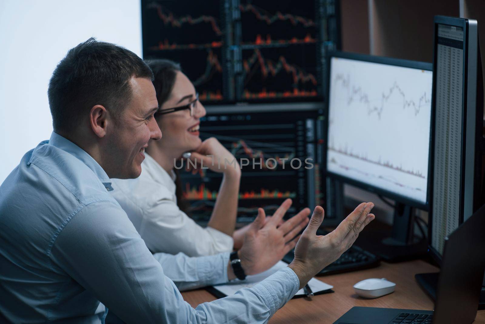 Cheerful people have success. Team of stockbrokers are having a conversation in a office with multiple display screens.