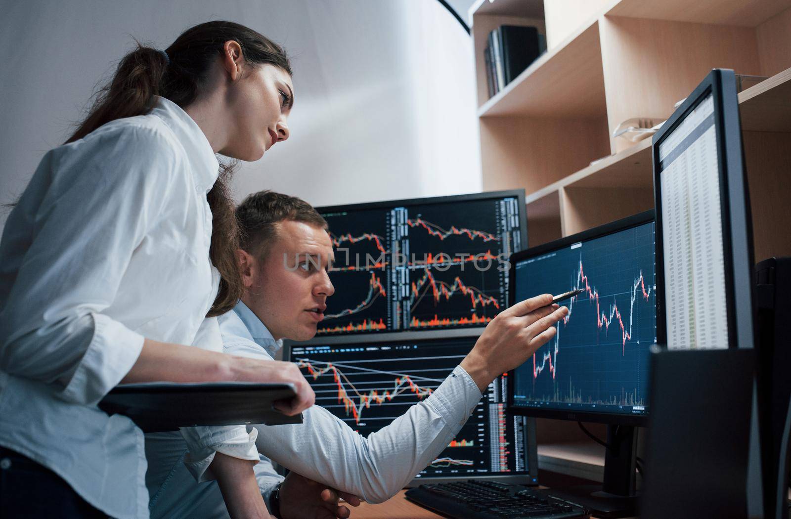 Team of stockbrokers are having a conversation in a office with multiple display screens.