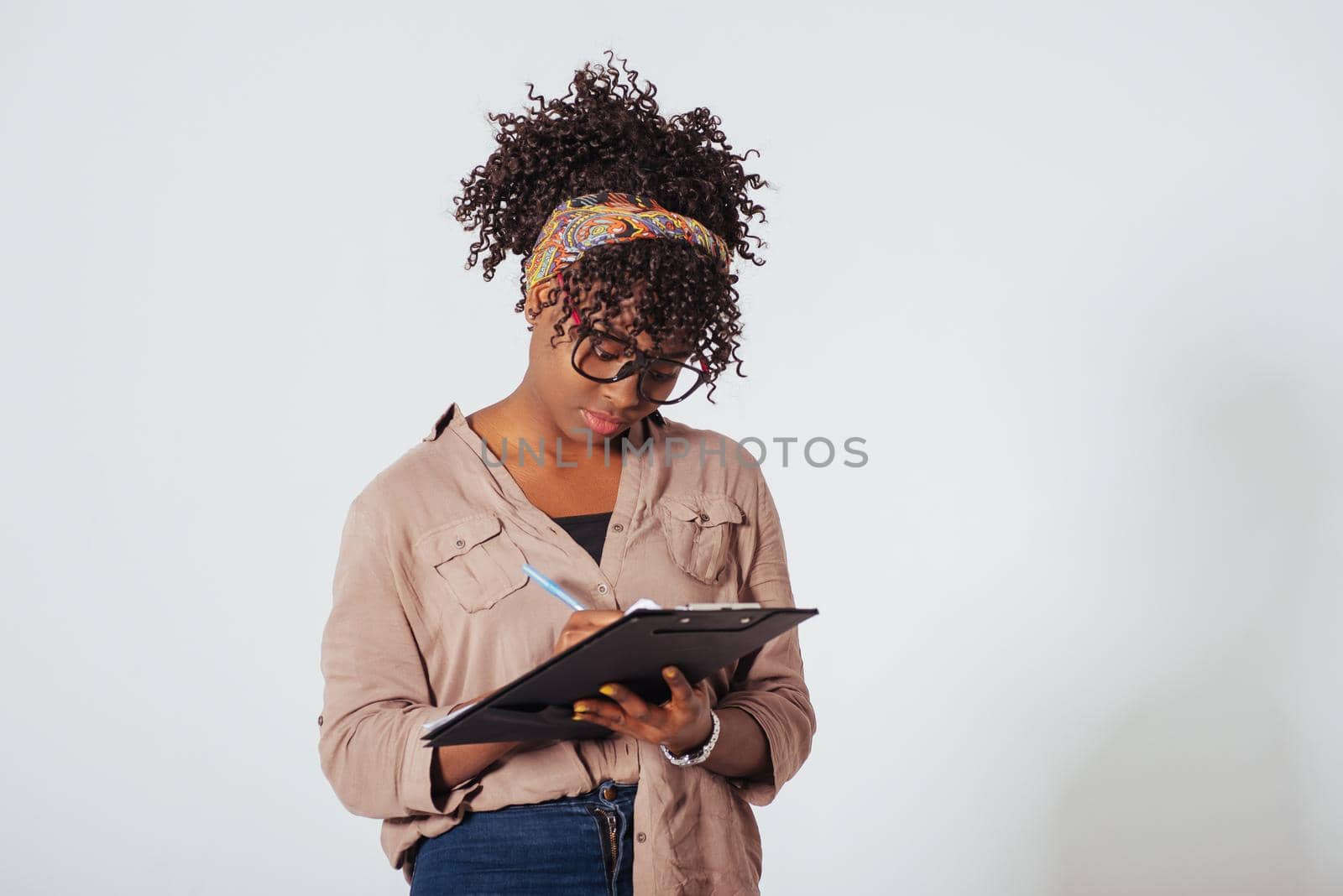 Student writes on the notepad. Beautiful afro american girl with curly hair in the studio with white background.