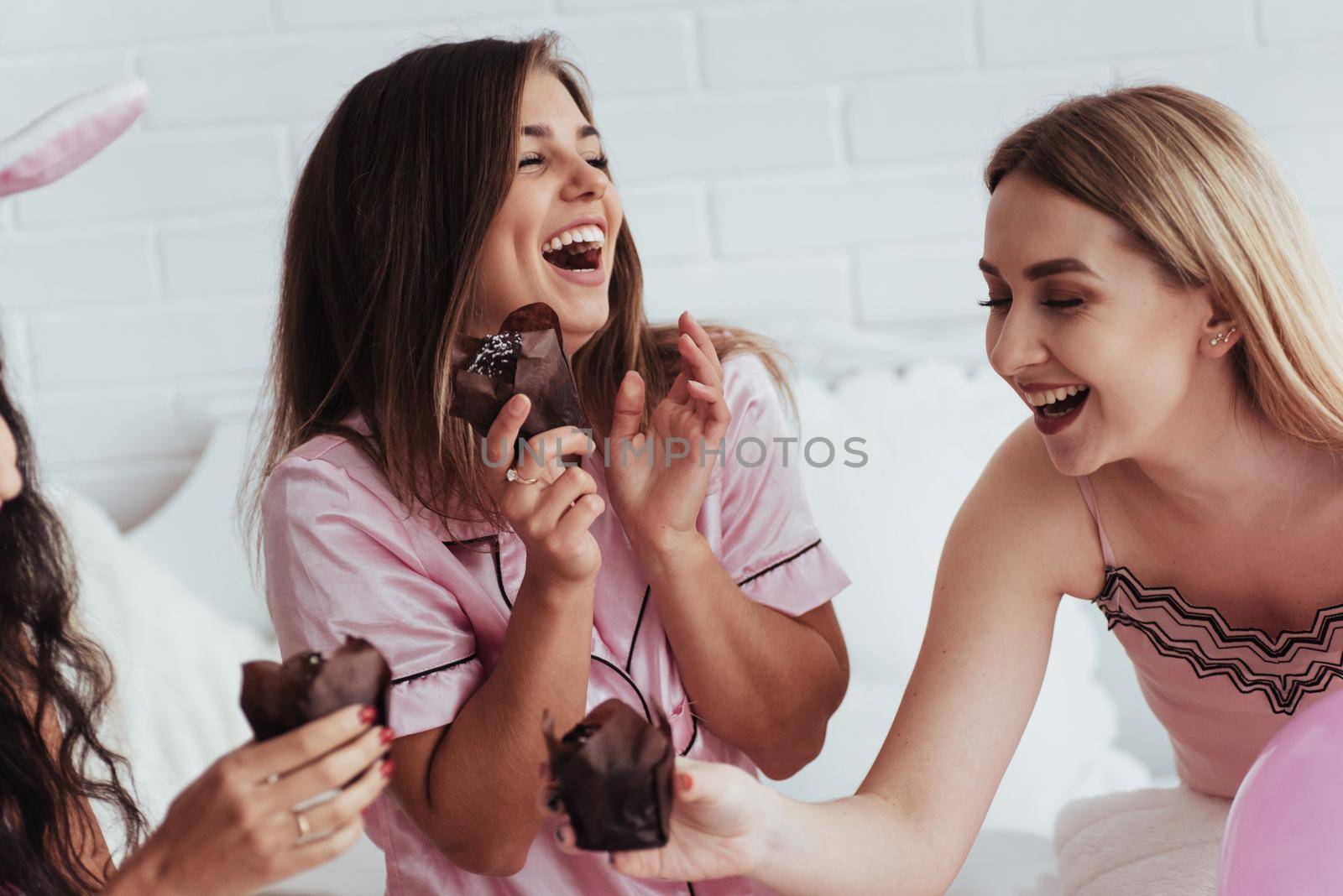 Sincere smiles. Bachelorette party in the bedroom. Delicious looking chocolate cookies at the girlish day. Four women in night wear.
