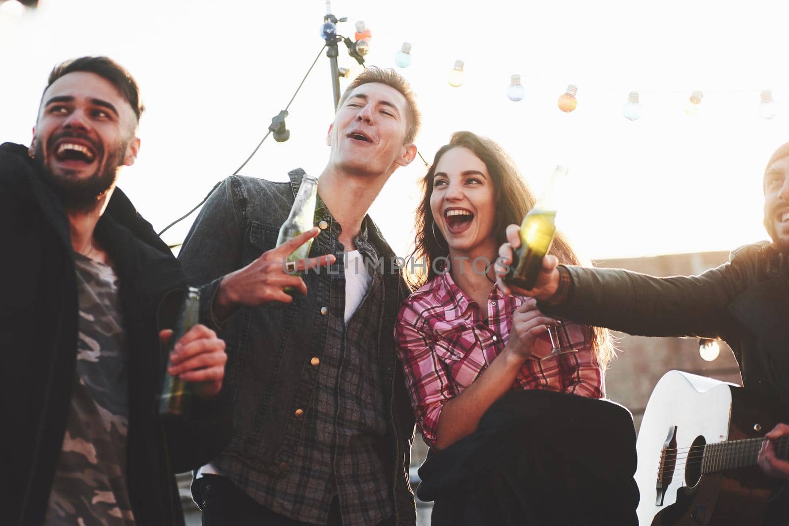 Gesturing and smiling. Group of young cheerful friends having fun while takes selfie on the roof with decorate light bulbs.