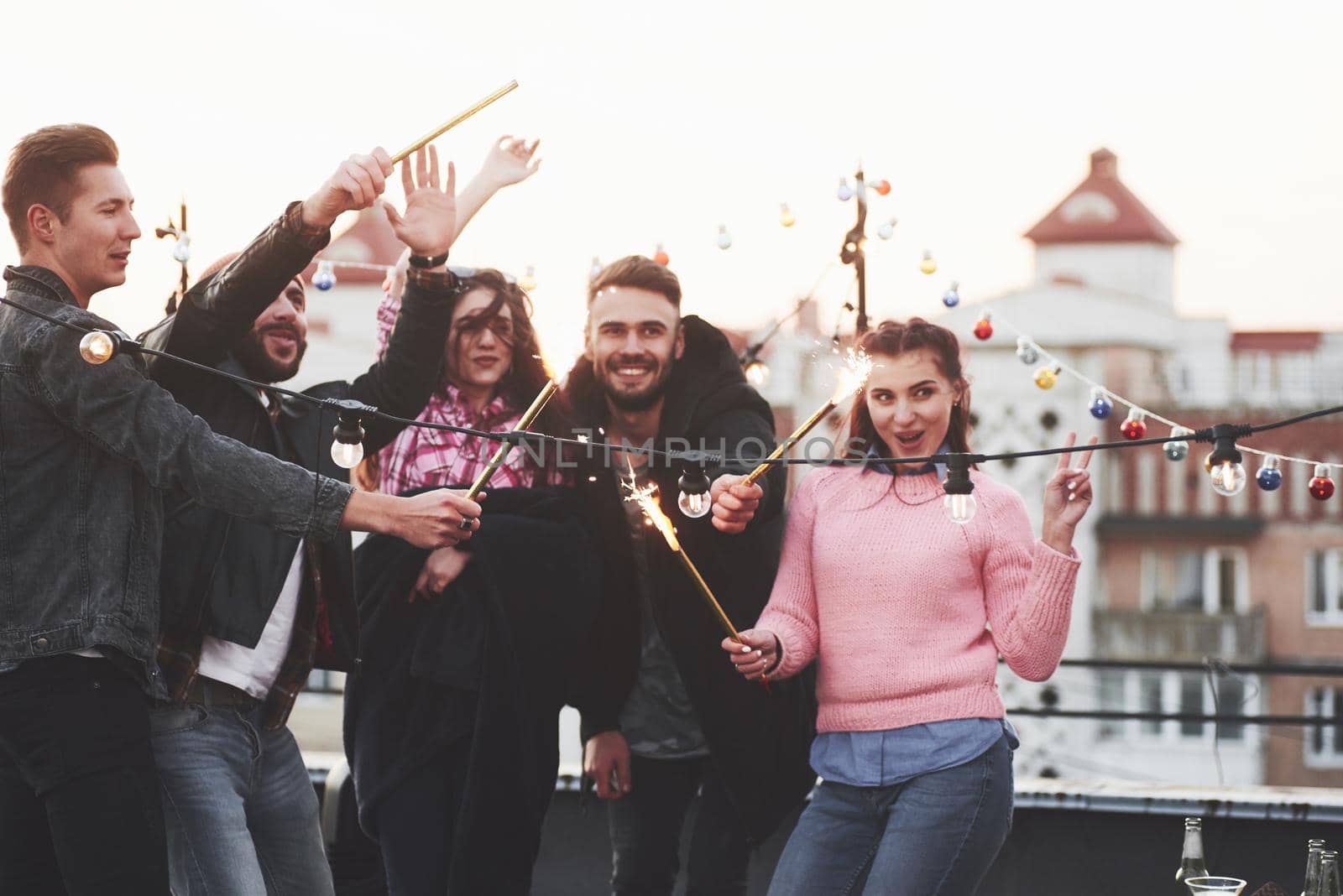 Girl showing gesture for the picture. Playing with sparklers on the rooftop. Group of young beautiful friends.