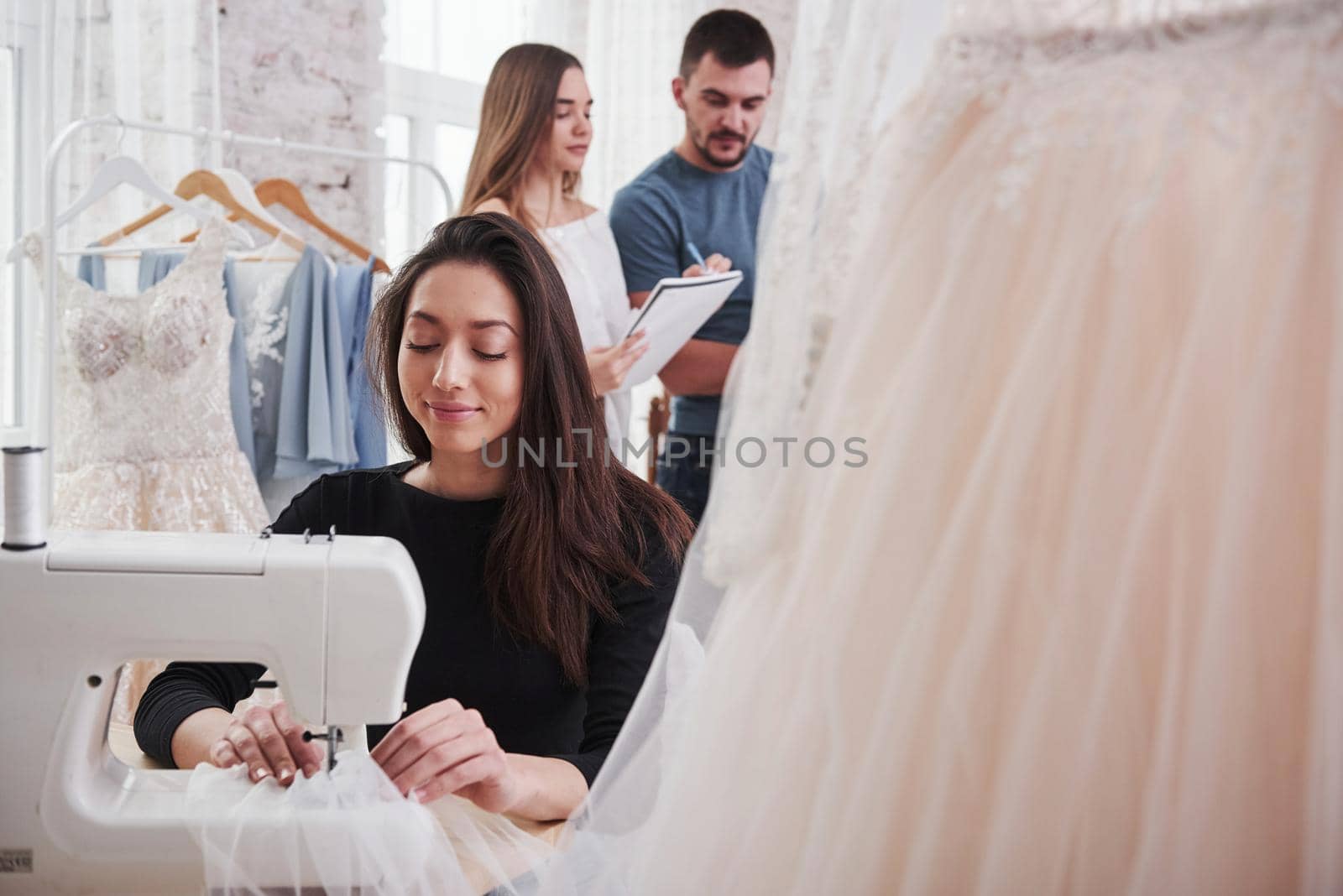 Employees makes calculations for an order behind. Female fashion designer works on the new clothes in the workshop by Standret