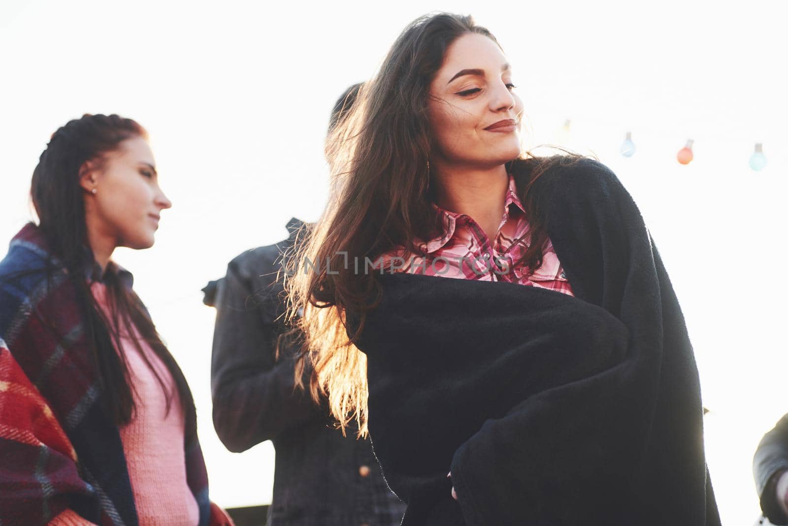 Girl is wearing warm clothes. It's rooftop party. Group of friends have holidays at sunny autumn day.