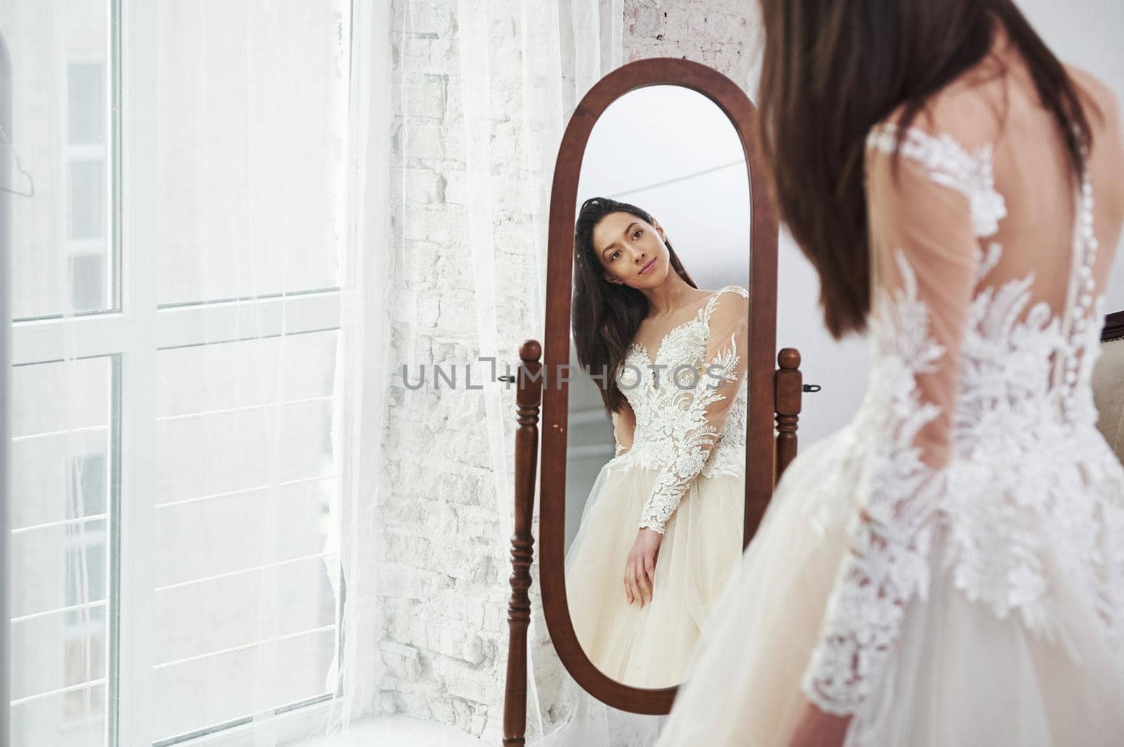 Young bride looks in the mirror. The process of fitting the dress in the studio of hand crafted clothes.