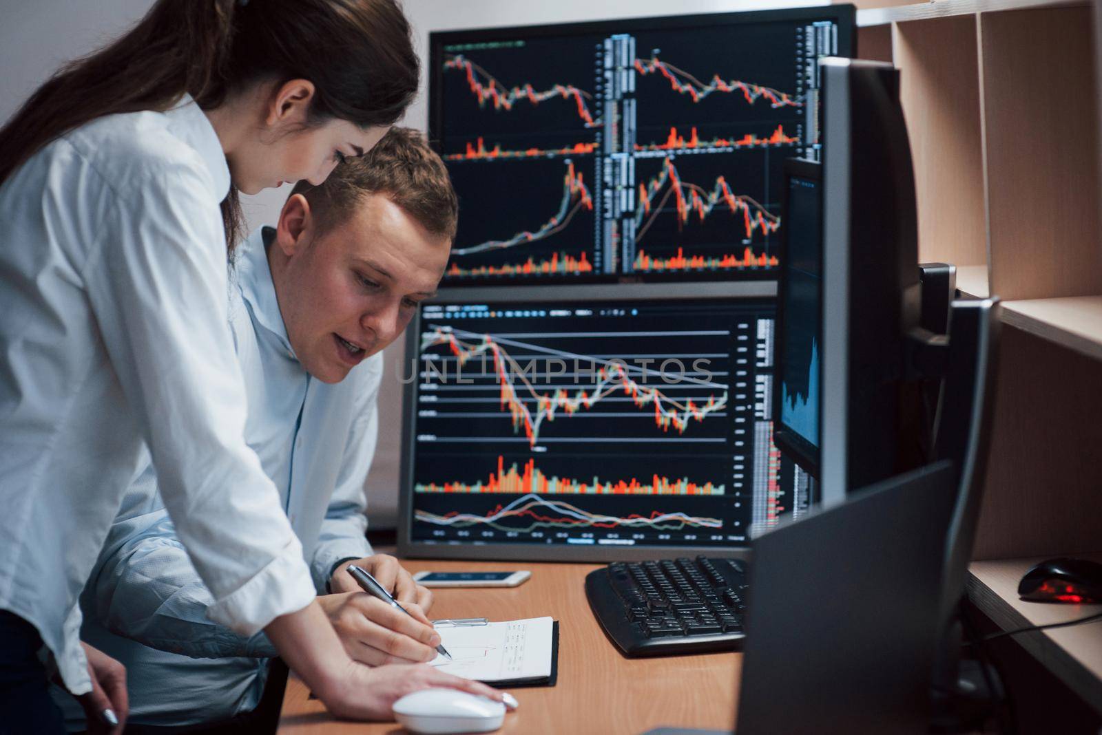 High and nice results. Team of stockbrokers are having a conversation in a office with multiple display screens.