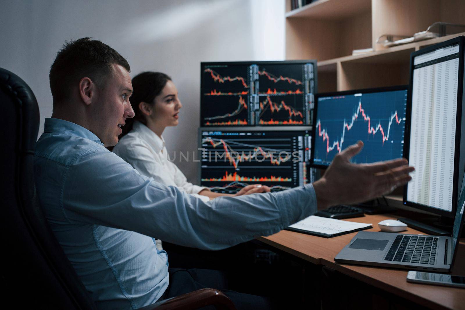 Team of stockbrokers are having a conversation in a office with multiple display screens.
