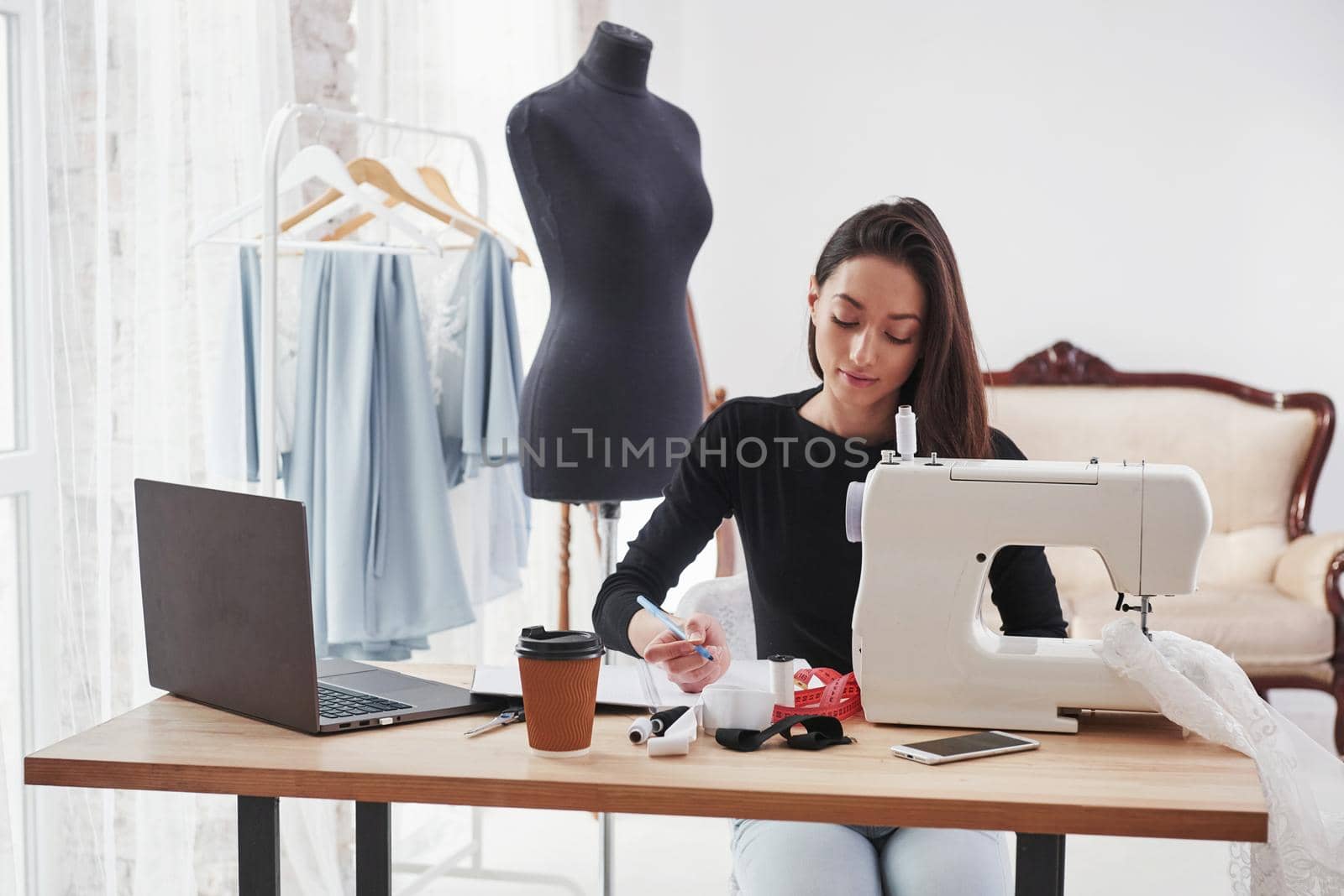 Does some calculations. Female fashion designer works on the new clothes in the workshop.