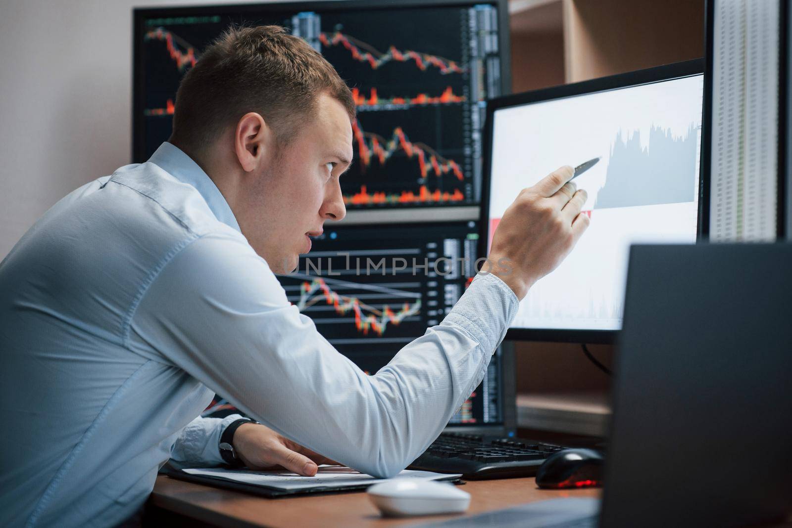 Making notifications of the project. Man working online in the office with multiple computer screens in index charts.