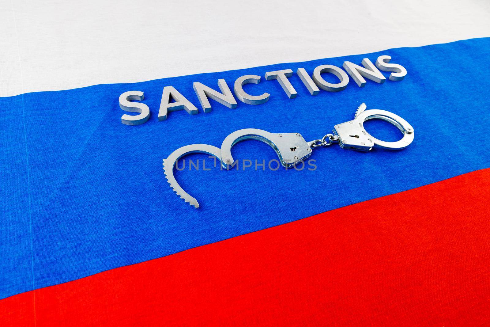 the word sanctions laid with silver metal letters on russian tricolor flag near handcuffs over it in directly above view