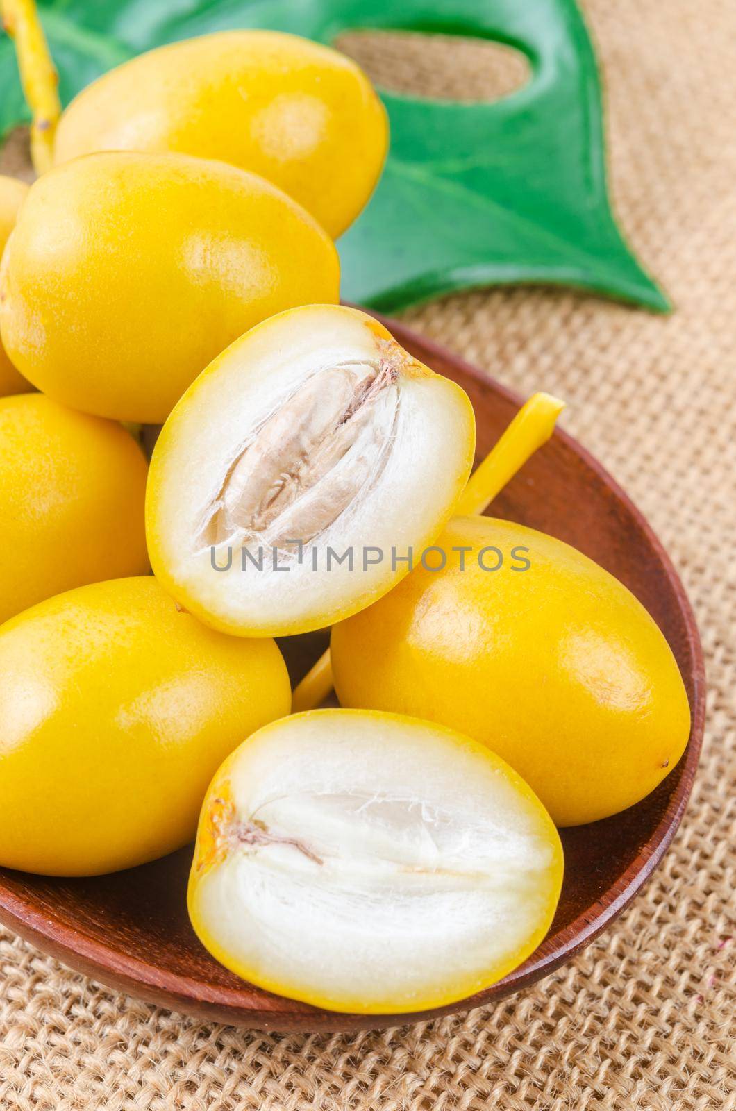 Fresh date palm fruits with green leaf on wooden background. by Gamjai