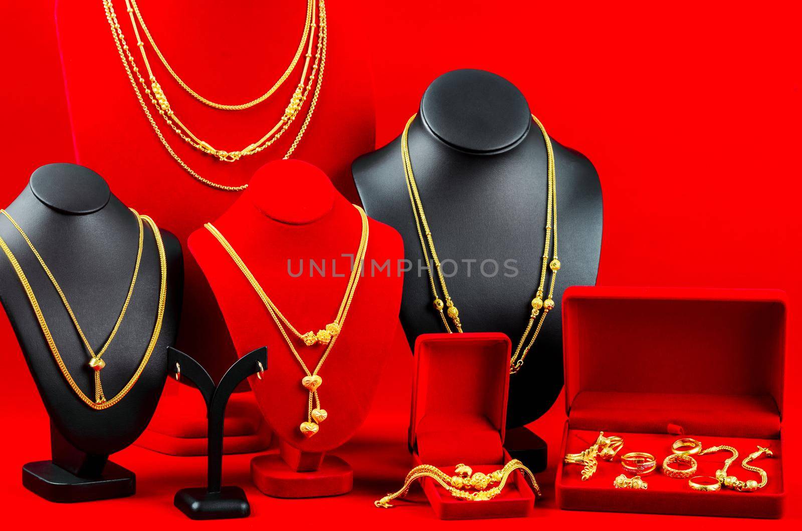 Accessory and gold jewelry necklace display stand with gold necklace on red Velvet fabric.