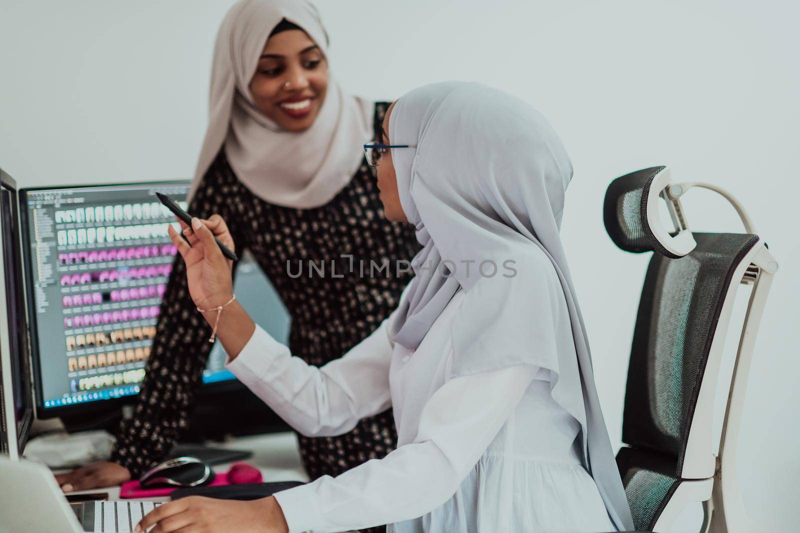 Friends at the office are two young Afro-American modern Muslim businesswomen wearing scarfs in a creative bright office workplace with a big screen. High-quality photo