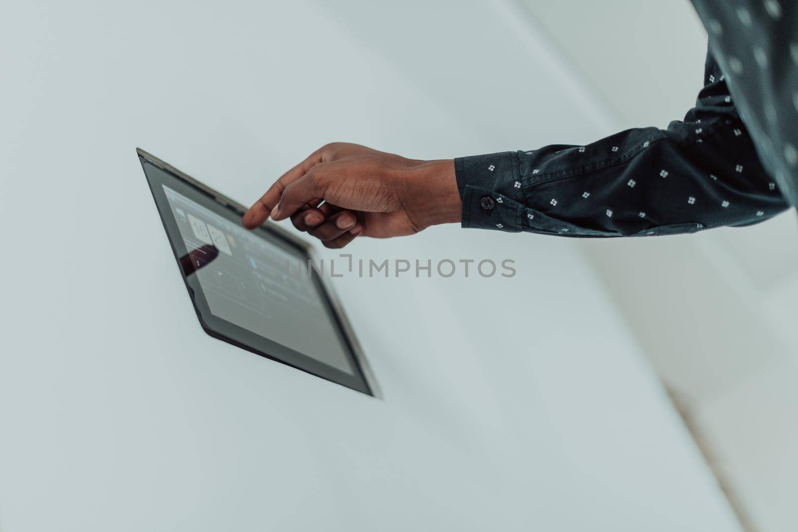 Smiling African American man using modern smart home system, controller on wall, positive young man switching temperature on thermostat or activating security alarm in apartment by dotshock