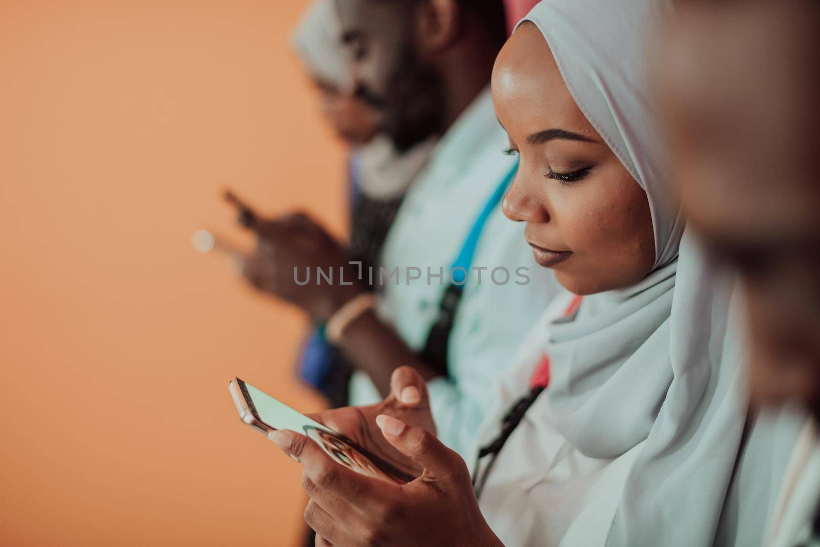 A group of African Muslim students use smartphones while standing in front of a yellow background by dotshock