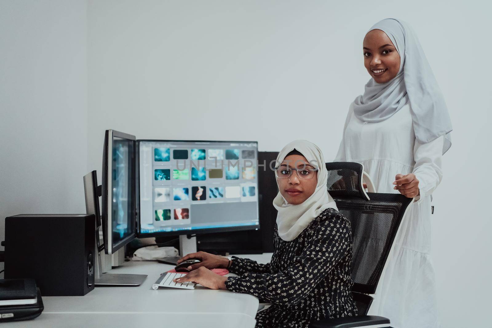 Friends at the office are two young Afro-American modern Muslim businesswomen wearing scarfs in a creative bright office workplace with a big screen. High-quality photo