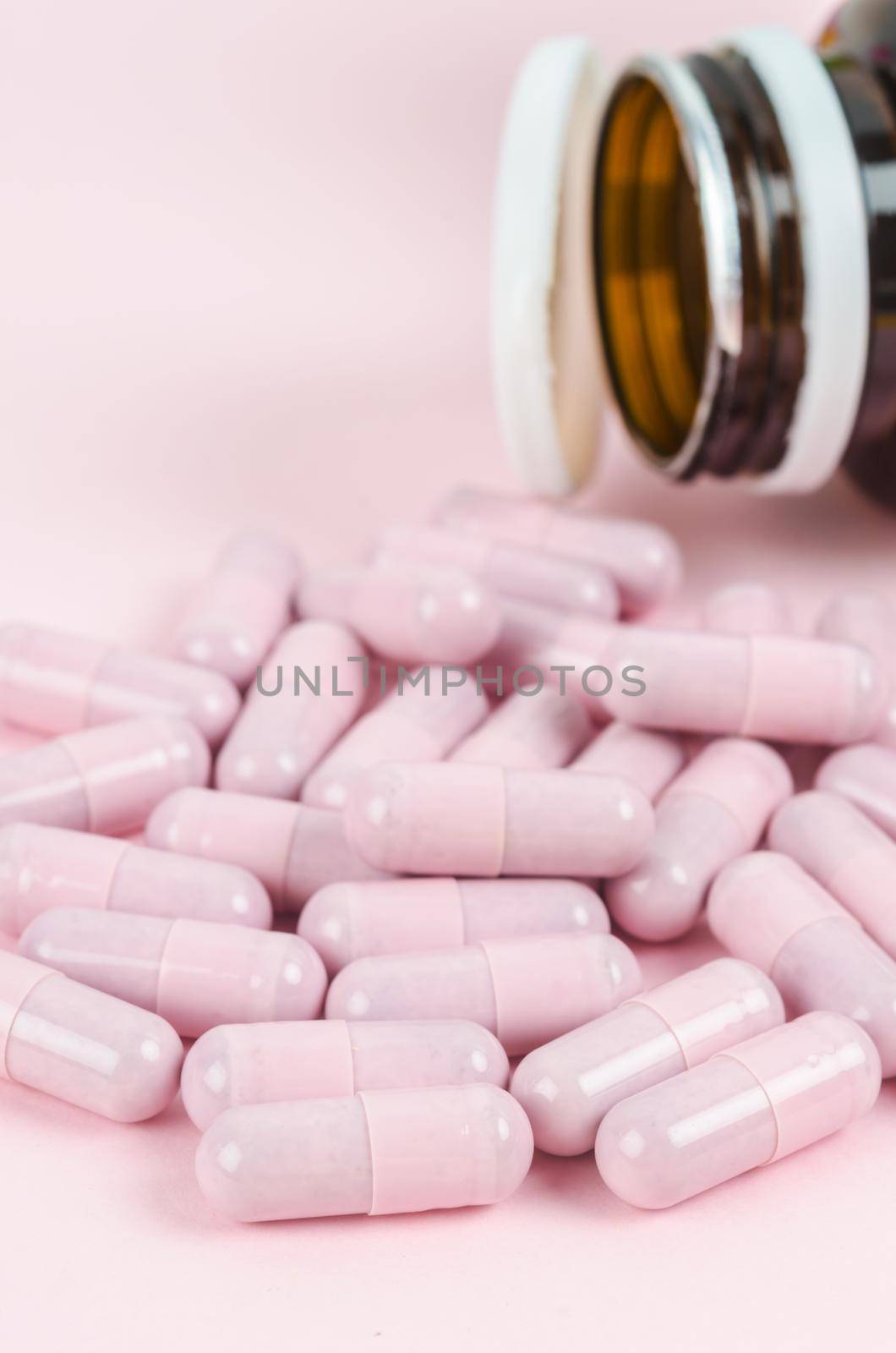 Pink capsule pills with bottle on pink background by Gamjai