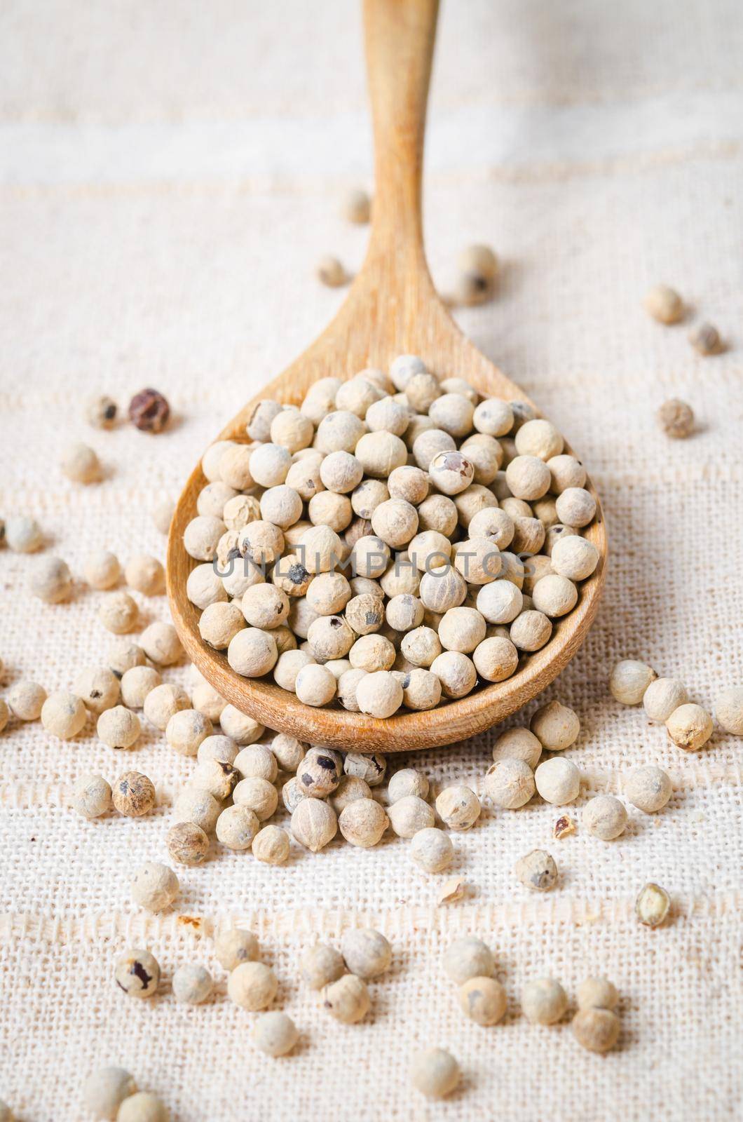 The White pepper seeds (peppercorn) in wooden spoon on tablecloth background.