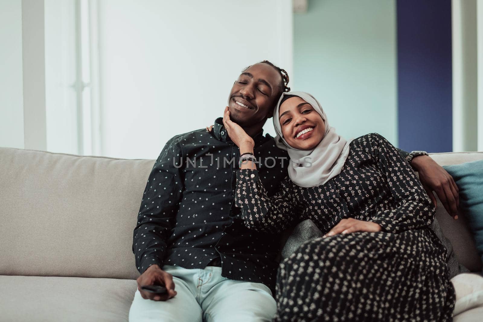 African Couple Sitting On Sofa Watching TV Together. Woman Wearing Islamic Hijab Clothes by dotshock