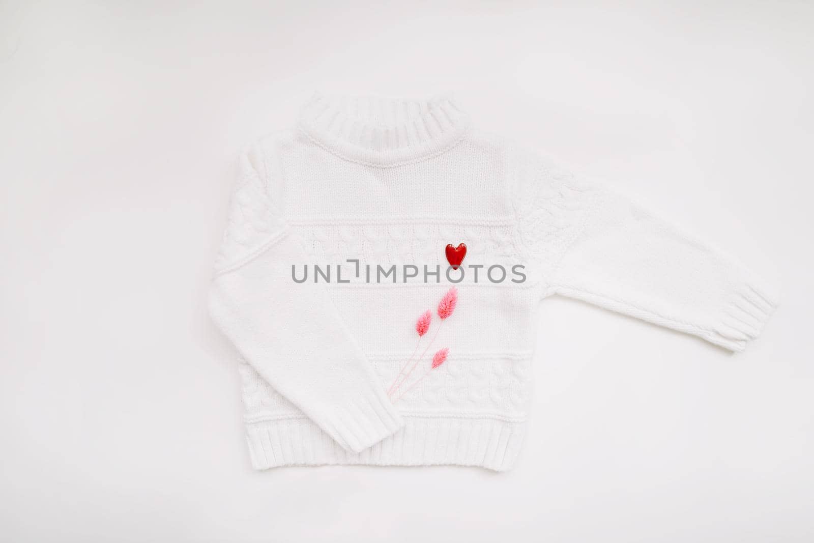 White woolen sweater with a red heart shaped pin on white background top view. Love, romance, fashion concept. Flat lay, copy space.