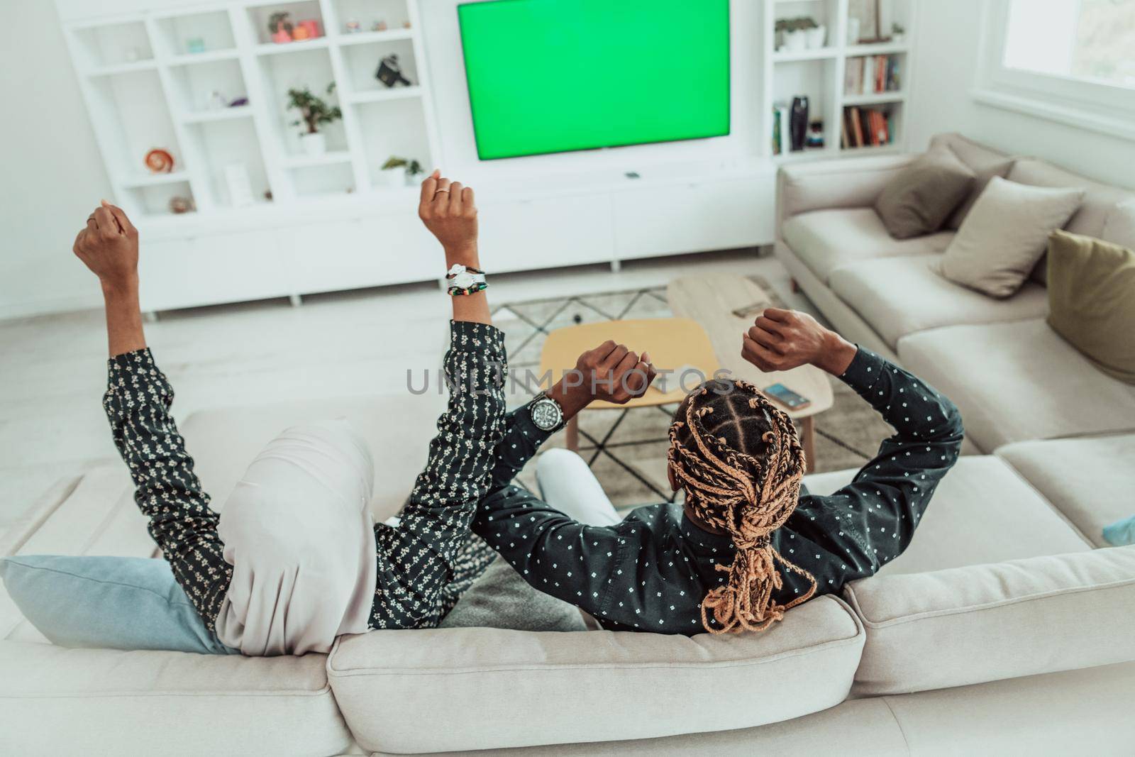 African Couple Sitting On Sofa Watching TV Together Chroma Green Screen Woman Wearing Islamic Hijab Clothes. High quality photo