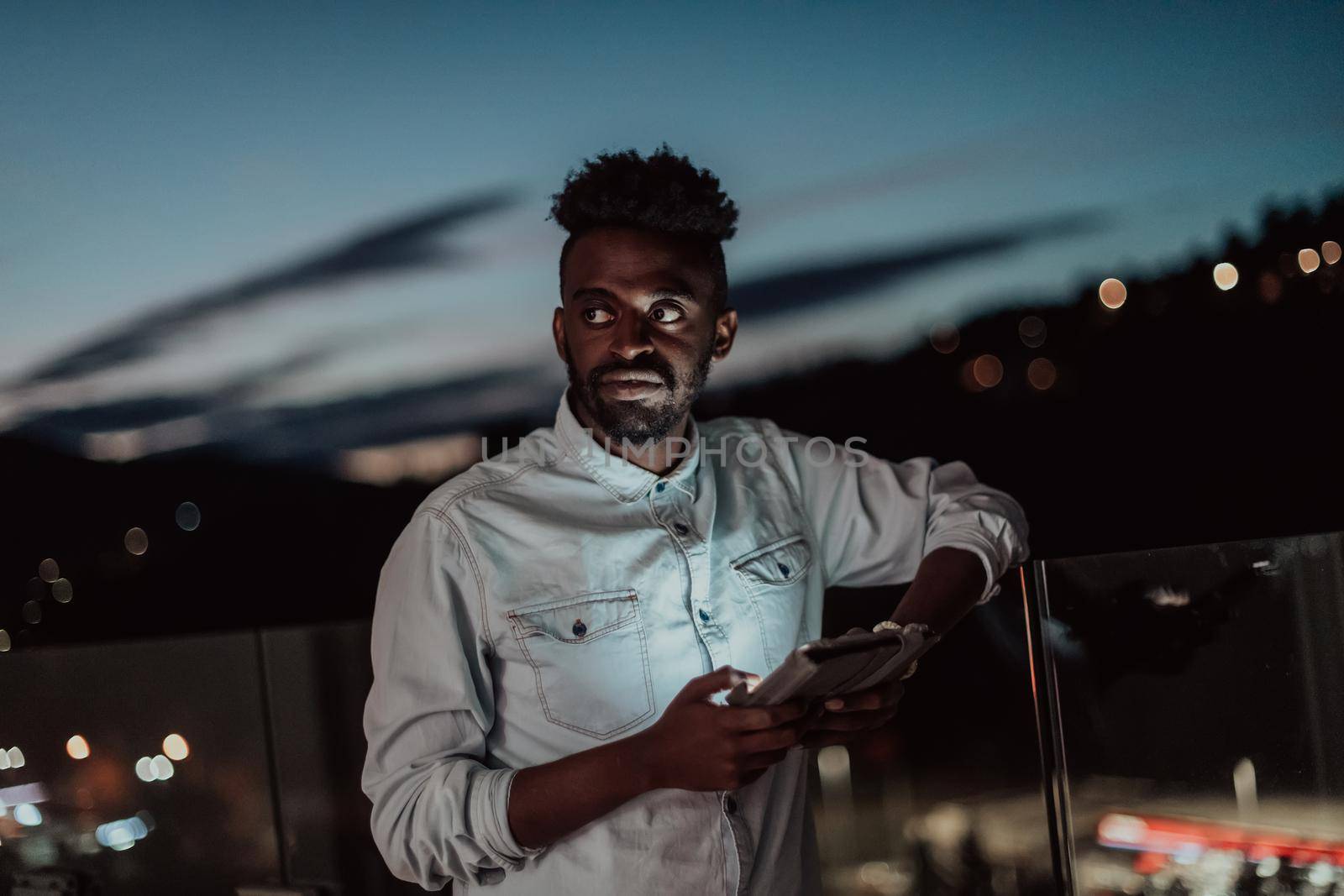 The young man on an urban city street at night texting on a smartphone with bokeh and neon city lights in the background. High-quality photo. High-quality photo