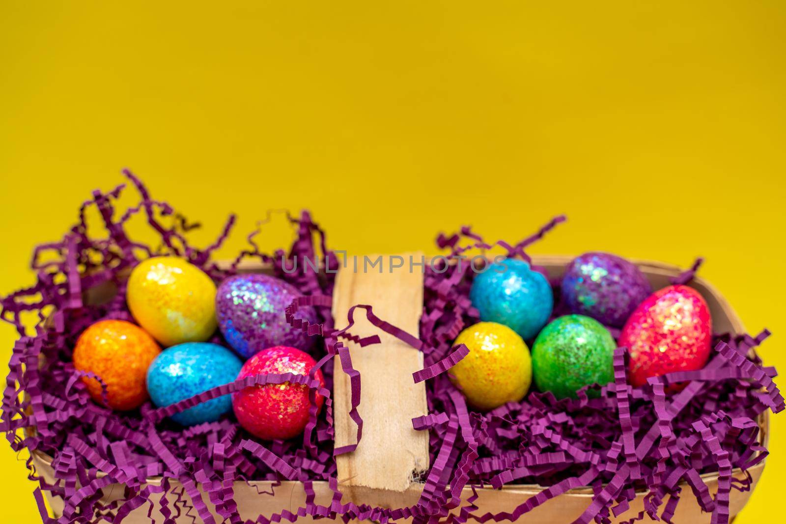 Easter composition from a basket and colored eggs prepared for the holiday on a yellow background.